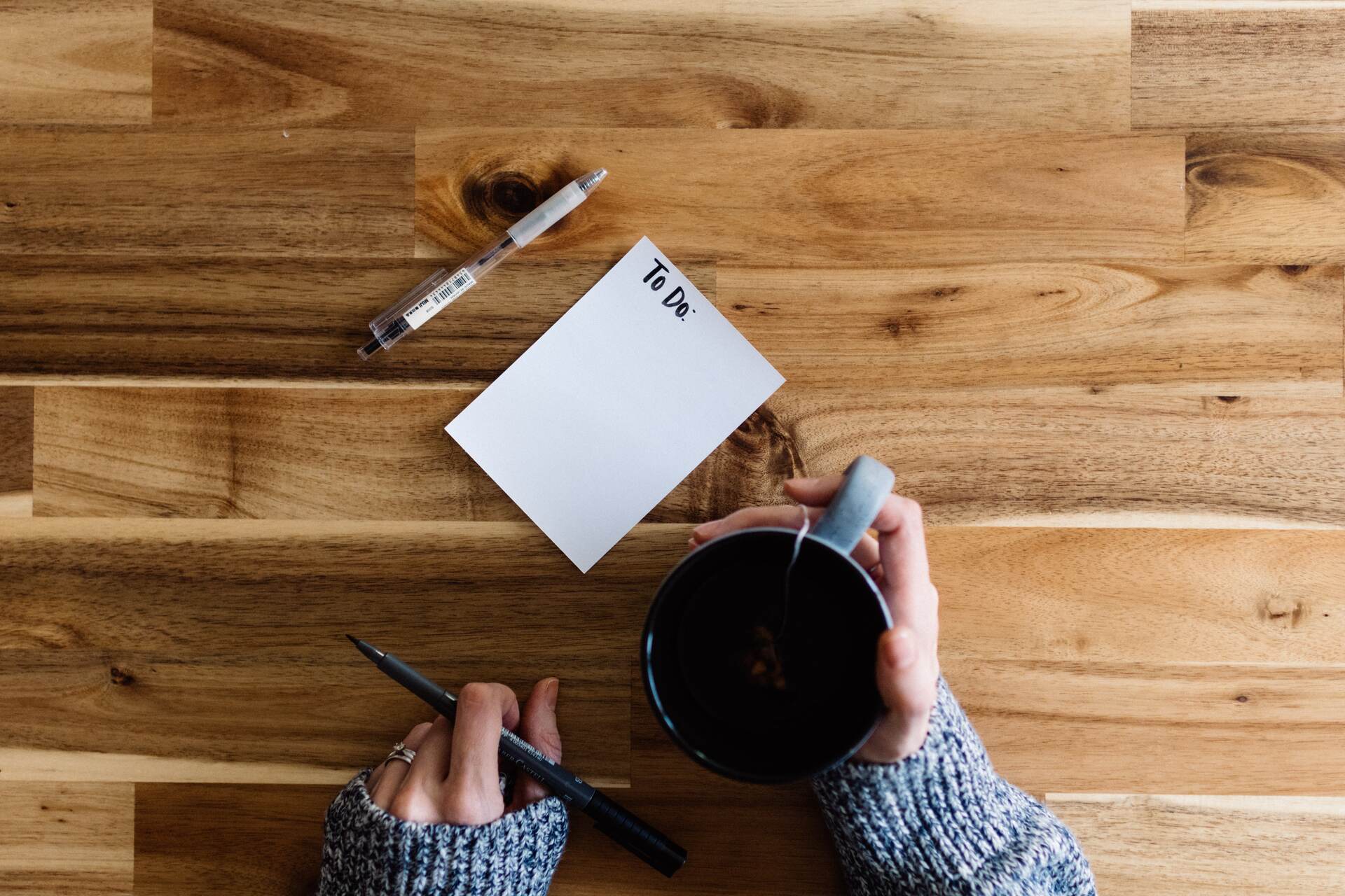 A person holding a mug and a pen with a to-do list for moving internationally before them
